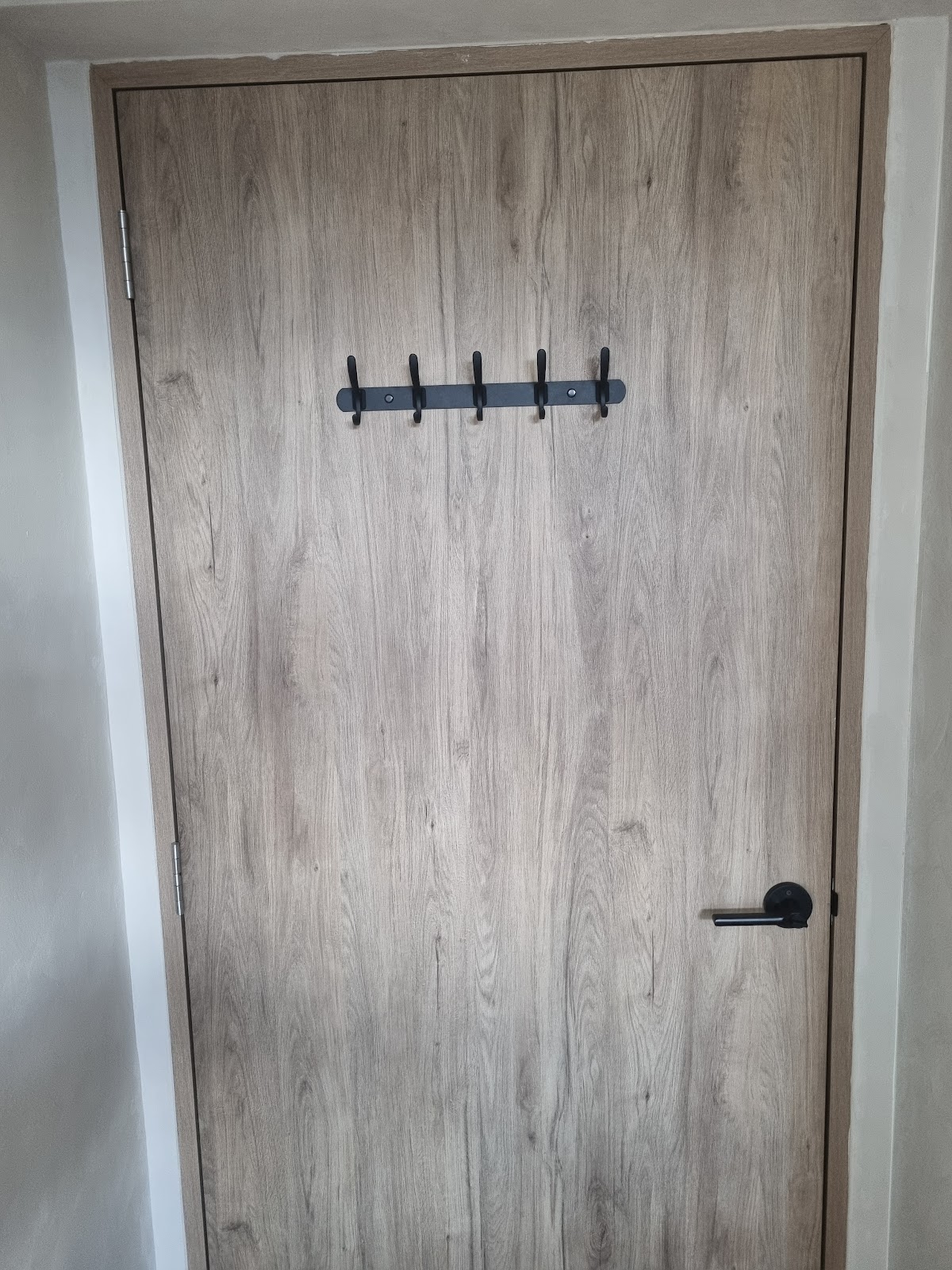 Black five hook coat rail mounted on a laminate door